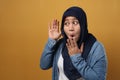 Portrait of Asian muslim woman smiling and doing hearing gesture, put hand on ear, listening carefully, over yellow Royalty Free Stock Photo