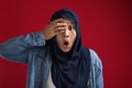Portrait of Asian muslim woman worried, shocked worried and peeking through her fingers, against red Royalty Free Stock Photo