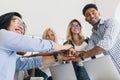 Portrait of asian office worker in glasses holding hands with adrican and european colleagues. Indoor photo of