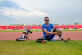 portrait of an Asian paralympic athlete, seated on a stadium track, busily affixing his running blades, preparing for intense