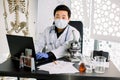 Portrait of Asian scientist doctor man sitting at the table and making notes on laptop, working with microscope and test Royalty Free Stock Photo