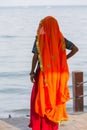 Portrait of Asian senior beautiful woman wearing traditional orange Indian dress sari. Near the beach, from behind