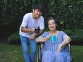 Asian senior woman sitting on wheelchair, drinking coffee or tea with her son in the garden. looking at camera, smiling happily Royalty Free Stock Photo