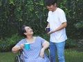 Asian senior woman sitting on wheelchair, drinking coffee or tea with her son in the garden. smiling happily Royalty Free Stock Photo