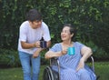 Asian senior woman sitting on wheelchair, drinking coffee or tea with her son in the garden. smiling happily Royalty Free Stock Photo