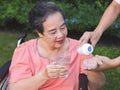 Asian senior woman sitting on wheelchair holding glass of water, get medical pill from her son. garden, outdoor Royalty Free Stock Photo