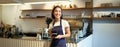 Portrait of asian smiling female barista, cafe waitress holding cup of coffee, serving clients, taking order to the Royalty Free Stock Photo