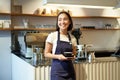 Portrait of asian smiling female barista, cafe waitress holding cup of coffee, serving clients, taking order to the Royalty Free Stock Photo