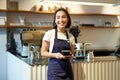 Portrait of asian smiling female barista, cafe waitress holding cup of coffee, serving clients, taking order to the Royalty Free Stock Photo