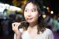 Portrait of Asian solo hipster traveller holding a fried roasted insect stick on street in Bangkok, Thailand. Female