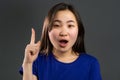 Portrait of asian thinking woman having idea moment pointing finger up on grey studio background. Smiling happy girl Royalty Free Stock Photo