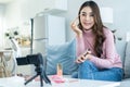 Portrait of Asian vlogger look at camera after review cosmetic at home. Beautiful Beauty blogger Influencer girl sit on sofa and