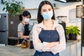 Portrait of Asian waitress stand with confident and cross arm in cafe. Attractive young beautiful girl barista in apron wear mask Royalty Free Stock Photo