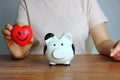 Portrait Asian woman holding red heart in hand with black and white piggy bank on wood table , saving money concept Royalty Free Stock Photo