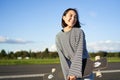 Portrait of asian woman with longboard. Korean girl skating, holding skateboard in hands, posing on road, smiling and Royalty Free Stock Photo