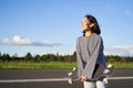 Portrait of asian woman with longboard. Korean girl skating, holding skateboard in hands, posing on road, smiling and Royalty Free Stock Photo