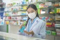 Portrait of asian woman pharmacist wearing a surgical mask using alcohol gel in a modern pharmacy drugstore, covid-19 and pandemic Royalty Free Stock Photo