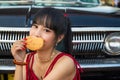 Portrait Asian woman in a red dress, she is hiding her mouth by cookies in front of a car