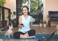 Asian woman wearing headphones, holding coffee cup, using mobile phone, sitting  on yoga mat in balcony  with computer laptop Royalty Free Stock Photo