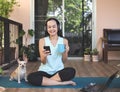 Asian woman wearing headphones, holding coffee cup, using smartphone, sitting  on yoga mat in balcony  with computer laptop Royalty Free Stock Photo