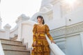 Portrait Asian woman wearing a yellow Thai patterned dress standing on a stair at a white Buddhis pagoda while traveling in Asia Royalty Free Stock Photo