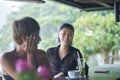 Portrait of 2 asian women chatting, drinking & smiling at beach bar in summer Royalty Free Stock Photo