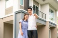 Portrait of Asian young couple standing and hugging together and holding house key looking happy in front of their new house to