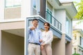 Portrait of Asian young couple standing and hugging together and holding house key looking happy in front of their new house to Royalty Free Stock Photo