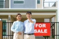 Portrait of Asian young couple standing and hugging together and holding house key looking happy in front of their new house to Royalty Free Stock Photo