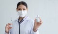 Portrait of Asian young doctor woman holding showing Covid-19 vaccines vial bottle in hand with face mask, stethoscope and syringe Royalty Free Stock Photo
