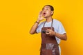 Portrait of Asian young man wearing apron holding game controller with open mouth shout encouraging isolated on yellow background