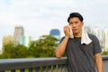 Portrait of Asian young man wearing sportswear, standing and wiping sweat with towel outdoor on walkway with city building Royalty Free Stock Photo
