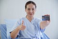 Portrait of Asian young patient woman holding blue credit card in her hand, smile and thumb up in other hand