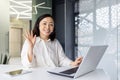 Portrait of an Asian young woman working in the office using a laptop, sitting at a desk in a headset, consulting and Royalty Free Stock Photo