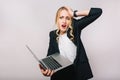 Portrait astonished busy young blonde woman working with laptop on white background. Talking on phone, mistake, upset