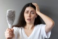 Portrait of a astonished caucasian young woman shows her hairbrush with losing hair. Gray background. The concept of Royalty Free Stock Photo