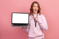 Portrait of astonished curly haired teenage girl in hoodie pointing finger at empty laptop copy space, looking surprised Royalty Free Stock Photo