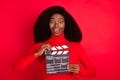 Portrait of astonished dark skin person open mouth hands hold clapboard isolated on red color background