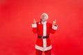 Portrait of astonished elderly man with gray beard wearing santa claus costume pointing and looking