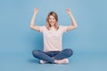 Portrait of astonished excited girl sit floor raise fists celebrate victory on blue background