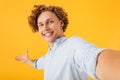 Portrait of astonished happy guy 20s taking selfie photo and holding copyspace on palm, isolated over yellow background