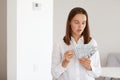 Portrait of astonished young adult beautiful girl wearing white casual style shirt, standing holding big sum of money, having Royalty Free Stock Photo