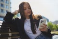 Beautiful young woman sitting on a bench in the city center and using a smart phone. Portrait of attractive brunette female