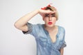 Portrait of attentive beautiful young woman in blue denim shirt with makeup and red headband standing with hand on forehead and