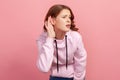 Portrait of attentive brunette teen girl in hoodie holding hand near ear trying to listen quiet conversation, overhearing gossip