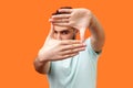 Portrait of attentive curious brunette man focusing through photo frame made of fingers. indoor studio shot on orange