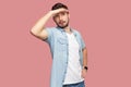 Portrait of attentive handsome bearded young man in blue casual style shirt standing with hand on forehead and looking away Royalty Free Stock Photo