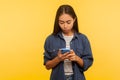 Portrait of attentive serious girl in stylish denim shirt typing message, dialing number calling on cell phone