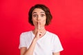 Portrait of attractive amazed curious girl showing shh sign oops isolated over vibrant red color background