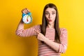 Portrait of attractive amazed funky girl demonstrating clock early morning over bright yellow color background